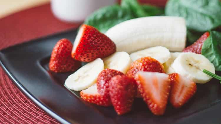 Closeup of spinach and cut strawberries and bananas on a black plate by a glass of milk, all that promote strong teeth